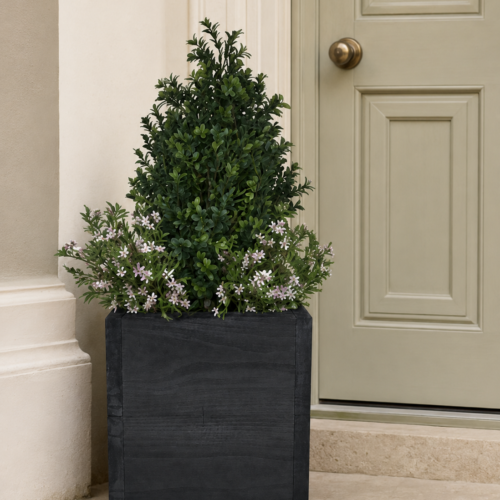 Artificial buxus shrub with pink flowers in a black timber planter beside a front door