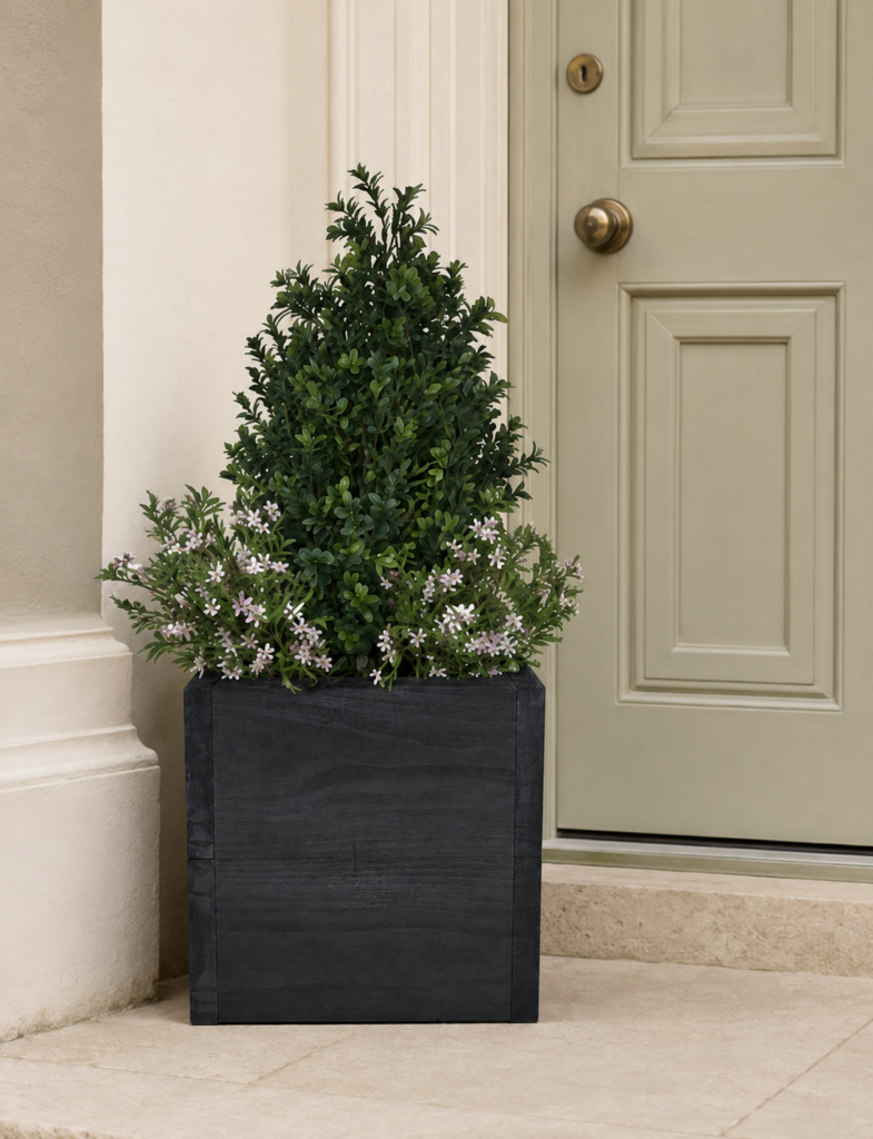 Artificial buxus shrub with pink flowers in a black timber planter beside a front door